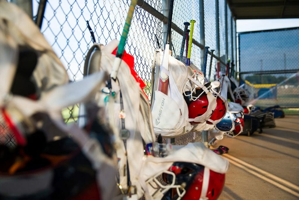 softball equipment bags hanging on a fence in the dugout